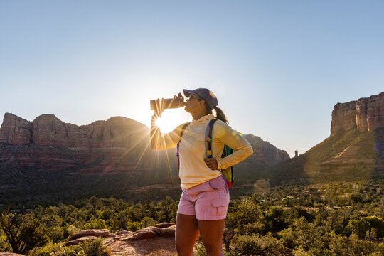 Female hiker drinking from water bottle with sunburst