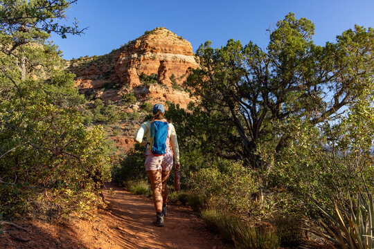Lone woman hiker walking away on high desert trail shrouded by brush