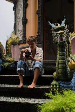Female photographer sitting by dragon statue at monastery, Bali