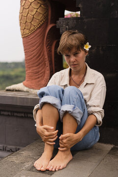 Pensive barefoot woman sitting at Balinese temple wall, Bali