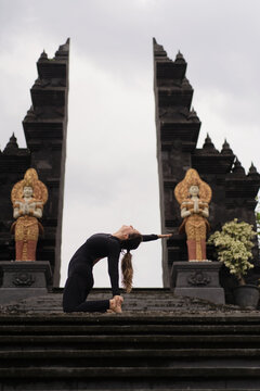 Woman performing camel pose yoga backbend at Balinese temple gate
