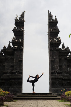 Woman in dancer yoga pose centered in Balinese gate with doves, Bali