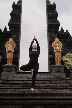 Woman in tree pose with hands in namaste at Balinese temple gate, Bali
