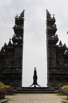 Woman in headstand pose centered in Balinese gate with doves on top