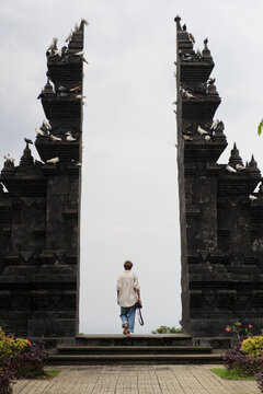 Woman photographer walking through Balinese temple gate with doves