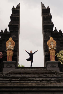 Woman in tree pose with open arms at Balinese temple gate, Bali