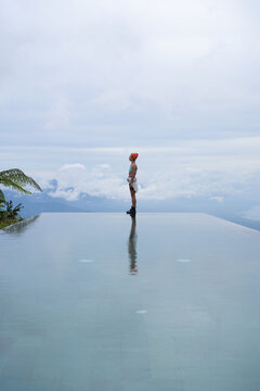 Young woman looking up at sky at infinity pool edge, Munduk, Bali