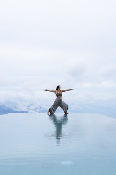 Woman in goddess yoga pose at infinity pool with mountain view, Bali