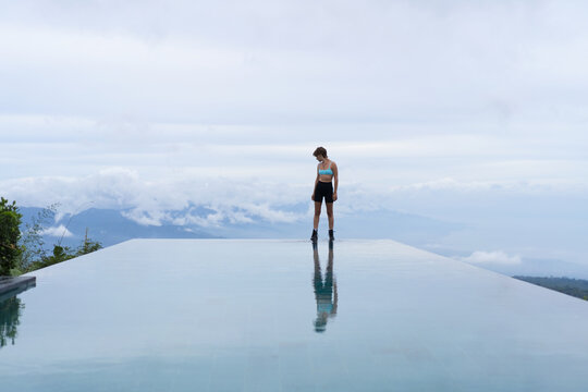 Pensive sporty woman at vast infinity pool with mountain view, Bali