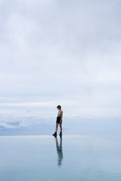 Solitary athletic woman at infinity pool edge under clouds, Bali
