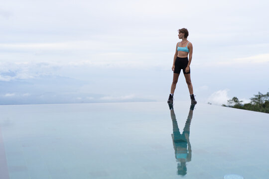 Sporty woman gazing at horizon from infinity pool edge, Munduk, Bali