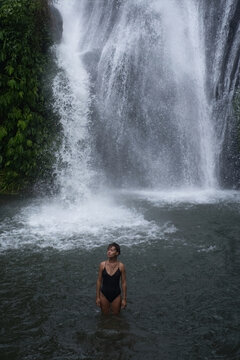 Woman looking up at Banyumala Waterfall from natural pool, Bali