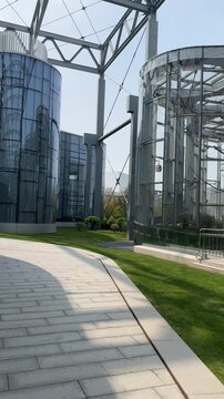 Modern glass cylinder towers with steel lattice canopy at Shanghai botanical complex, April 2026. Curved walkway and lush green lawn frame futuristic greenhouse architecture.