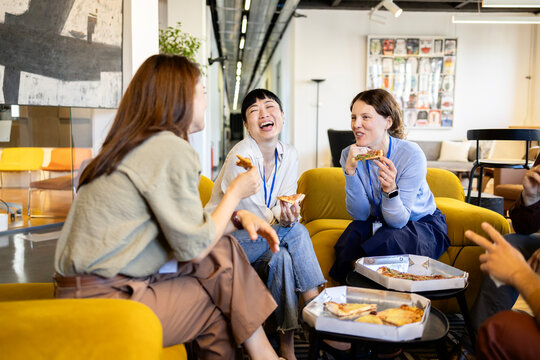 Multiethnic business team enjoying office pizza party, coworkers laughing and eating during casual lunch break