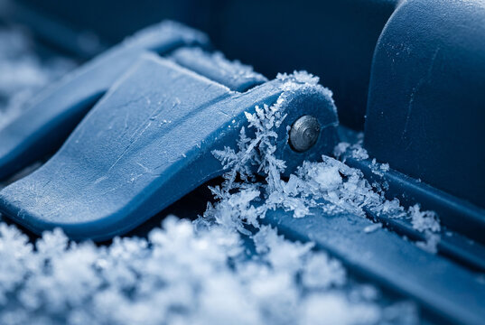 Macro extreme close-up of heavy frost accumulating on a rugged medical cooling box latch. The intricate ice crystals against the textured blue polymer highlight the material's durability and cryogenic