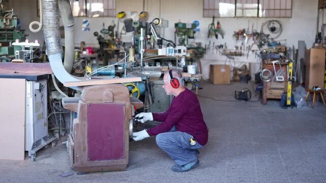 Senior carpenter operating thicknesser machine in his workshop