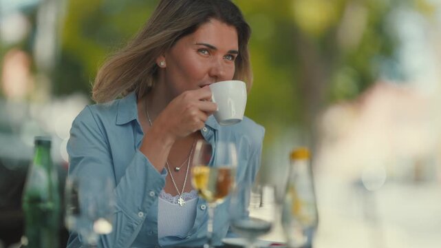 Woman enjoying drinks and food at an outdoor cafe in the city with trees on a sunny day