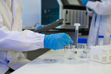 Fototapeta premium Scientist in Lab Coat and Blue Gloves Conducting Chemical Experiment with Beakers and Petri Dish in Laboratory