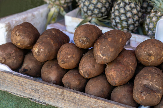 Wooden crate filled with dark brown bua hima root vegetables at a local market in Thailand, with fresh tropical produce displayed in the background.