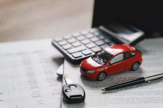 Red car model with calculator, vehicle key, pen, and financial documents on office desk representing car financing, auto loan calculation, insurance payment, and automobile ownership process.