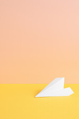 Naklejka premium Paper airplane on yellow surface with peach background, symbolizing creativity and imagination in bright, minimalistic setting