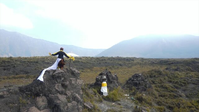 Traditional Balinese dancer performing on a rocky hill with mountain views in 4K.