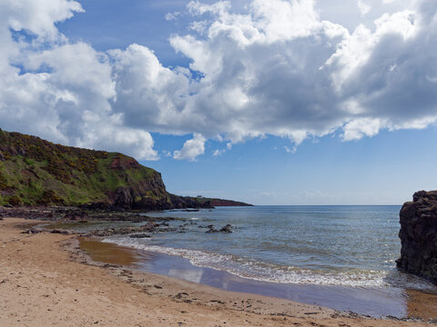 A small deserted bay between the rocks at the northern end of St Cyrus Beach with the calm water receding with the tide.