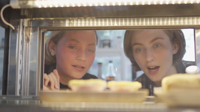 Bakery display window with young people choosing pastry, young woman and man looking into pastry case at bakery counter, women bakery pastry display window cafe food dessert selection shop
