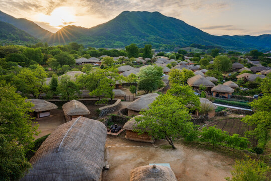Beautiful sunrise over Nagan Eupseong Folk Village in Suncheon, South Korea. Traditional Korean thatched houses and historical hanok village surrounded by green trees and mountains landscape.