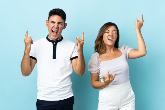 Young caucasian couple isolated on blue background making rock gesture