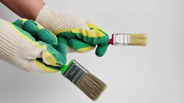 In close-up on a white background, two hands in work gloves hold paint brushes and twist them in different directions. The concept of repair, surface painting, paint. High quality 4k footage