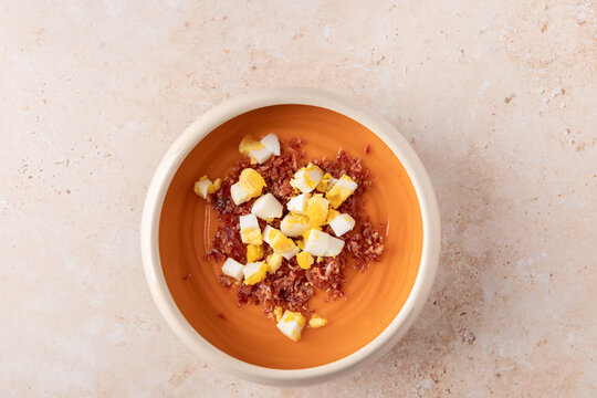 Horizontal top view of traditional homemade salmorejo with serrano ham and chopped egg in beige bowl on light stone background with copy space. Concept of Spanish cuisine and Mediterranean food