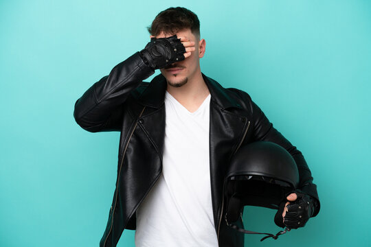 Young caucasian man with a motorcycle helmet isolated on blue background covering eyes by hands. Do not want to see something