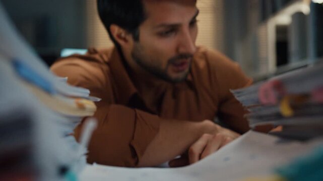 Overworked young Latin businessman waking from sleep nap to rush paperwork at desk in dark night office. Working late deadline burnout, heavy workload stress, and exhausted corporate problem concept.