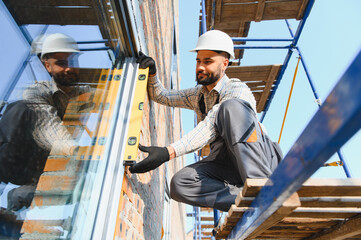 Obraz na płótnie Canvas Construction worker installing window using spirit level on scaffolding