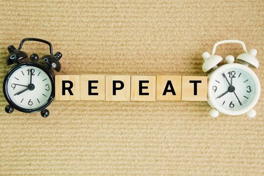 Alarm clock and wooden cube with the word Repeat. to say or do something again