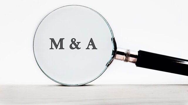 A magnifying glass on a white surface slowly clarifies partial letters into M  A. This visual represents understanding complex Mergers and Acquisitions in business