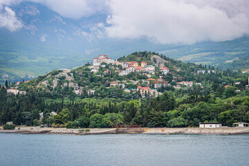 Fototapeta premium Mountains and buildings stand on a hillside by the water under cloudy skies