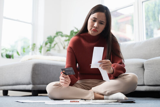 Financial crisis or debt concept, Young Asian woman feeling worry and stress after received many expense bill from expense usage. Asian woman feeling sad or worry about their financial situation.
