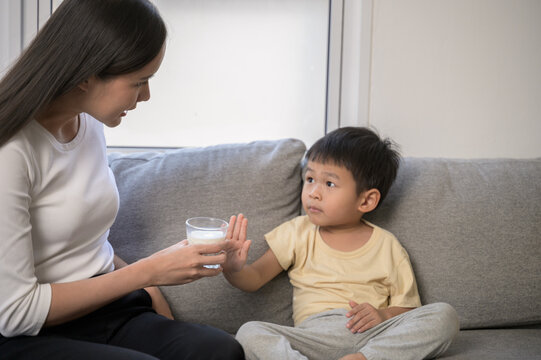 Adorable Asian baby boy using hand refuse drinking cow milk from his mother showing lack of appetite or picky eating behavior. Concept of child nutrition, food refusal, and parenting challenges.