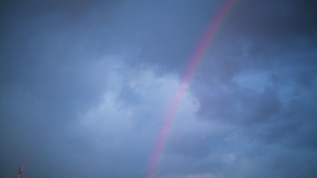 Partial rainbow visible through dense grey storm clouds in the sky, with soft gradient colors fading into the overcast background