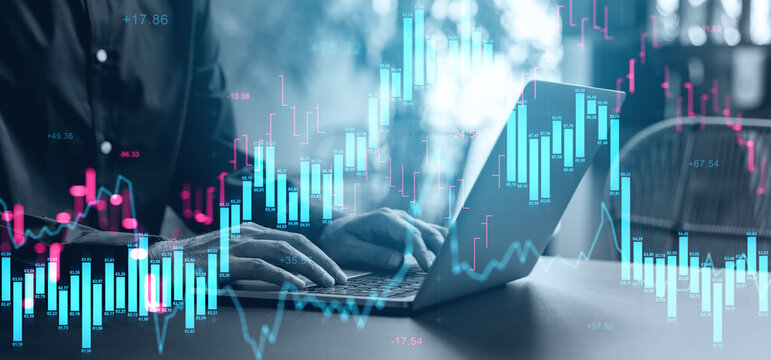 Hands typing on laptop with glowing candlestick chart overlay showing financial market activity and volatility in modern business environment..