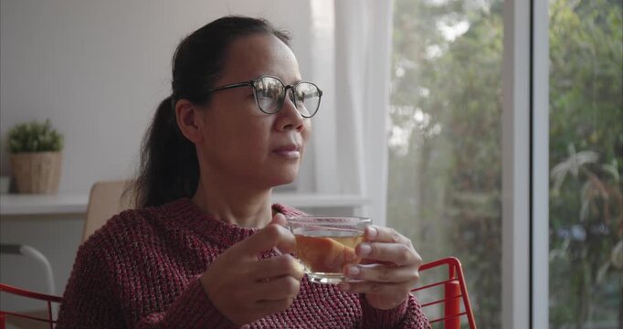 Asian Woman with glasses holding teacup by Window in Morning