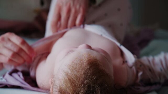 Close up top down view of a baby lying on a padded surface, wearing a light pink onesie with small dark patterns