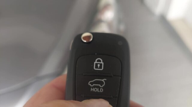 Close-up of a person holding a black car key fob with control buttons outdoors