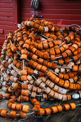 Fototapeta premium Close Up of Weathered Orange Fishing Net Floats Piled Against a Red Wooden Wall in Alaska
