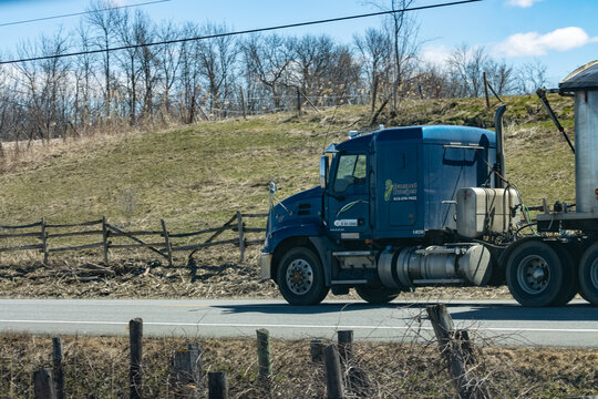 Quebec, Canada, 24 April 2026 : A blue Mack semi truck with a silver trailer drives on a rural road under a clear sky.