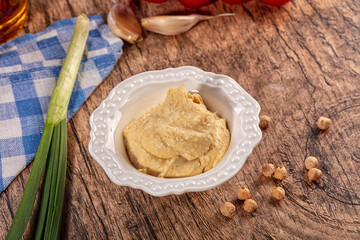 Fototapeta premium Creamy hummus bowl, fresh chickpeas, green onion, garlic on rustic wood