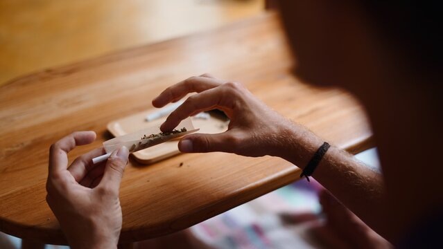 Person's hands rolling a cannabis joint on a wooden table