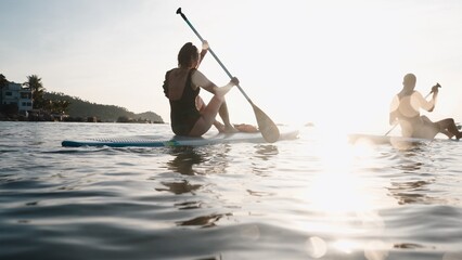 Fototapeta premium Couple paddleboarding enjoying tranquil ocean during tropical sunset vacation
